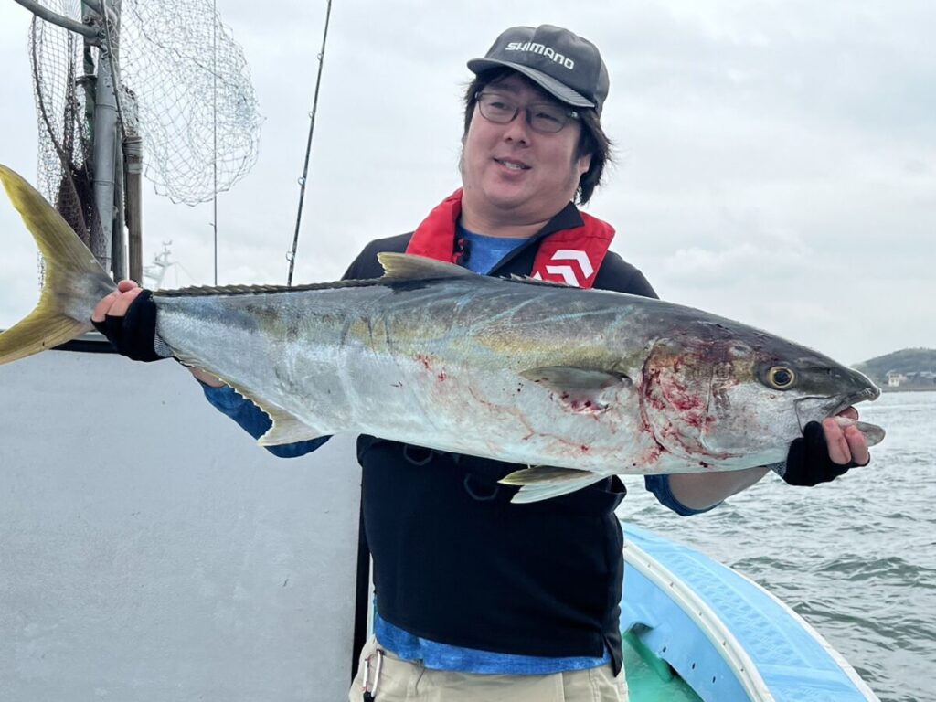 遊漁船の上で大きな魚を抱えながら微笑んでいます。