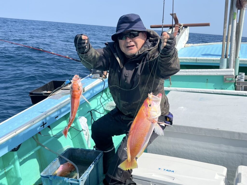 帽子とジャケットを着てボートに座っている人が、釣った魚を 2 匹持ち上げています。