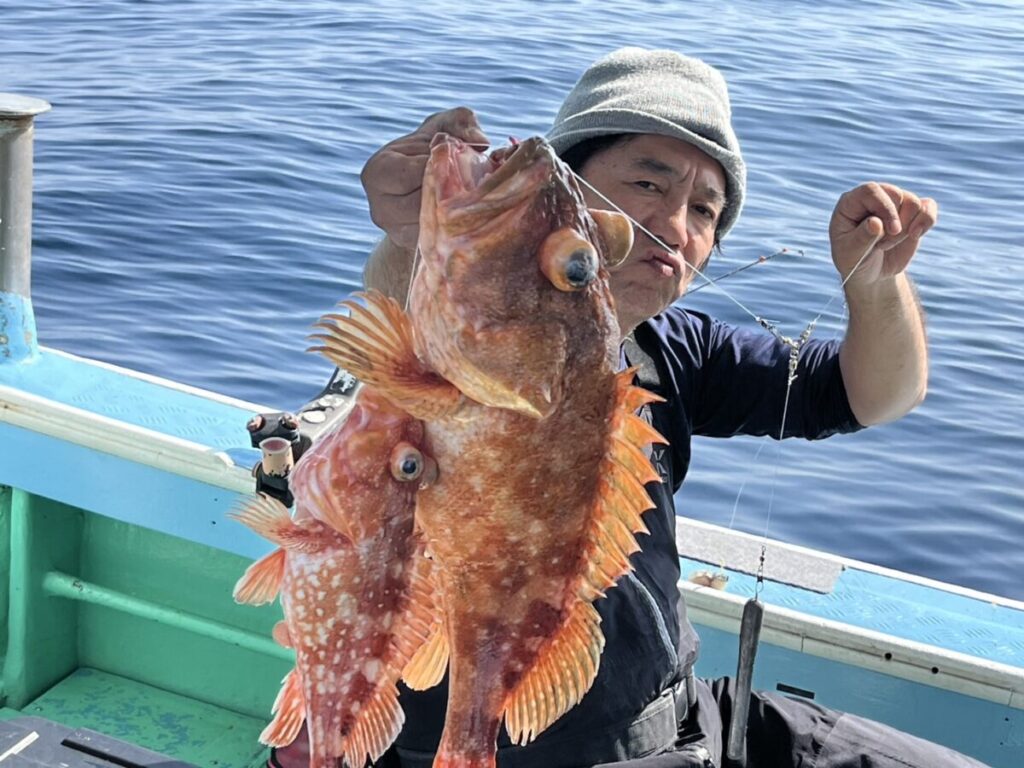 ボートに乗っている人が、静かな青い海を背景に、とがったひれを持つ、大きな魚を2匹掲げています。