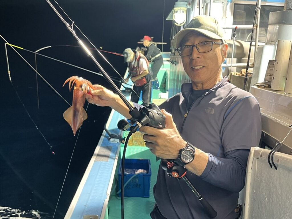 夜の船上で、片手に釣り竿、片手に釣りたてのイカを持つ男。