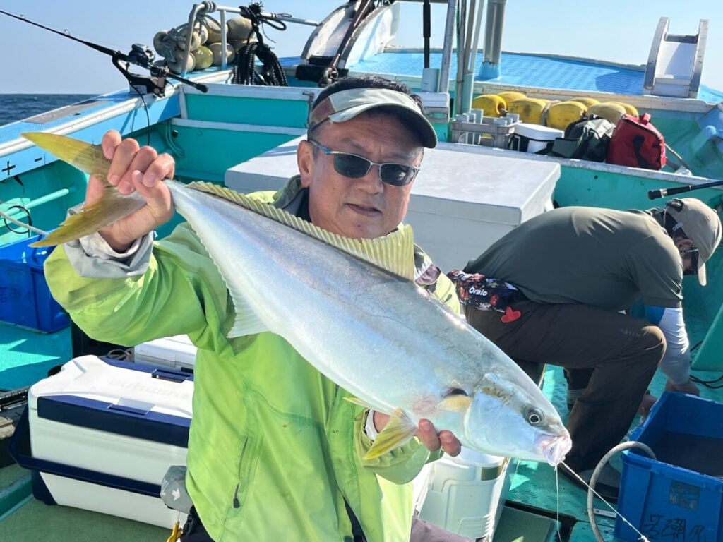 緑色のジャケットと帽子を身につけた人物が、ボートの上で大きな魚を手にしている。