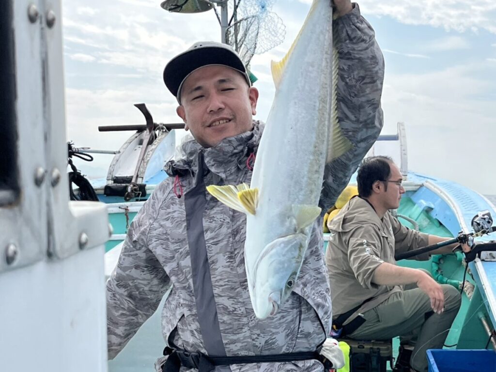 ボートに乗った男性が釣った大きな魚を掲げて微笑む。