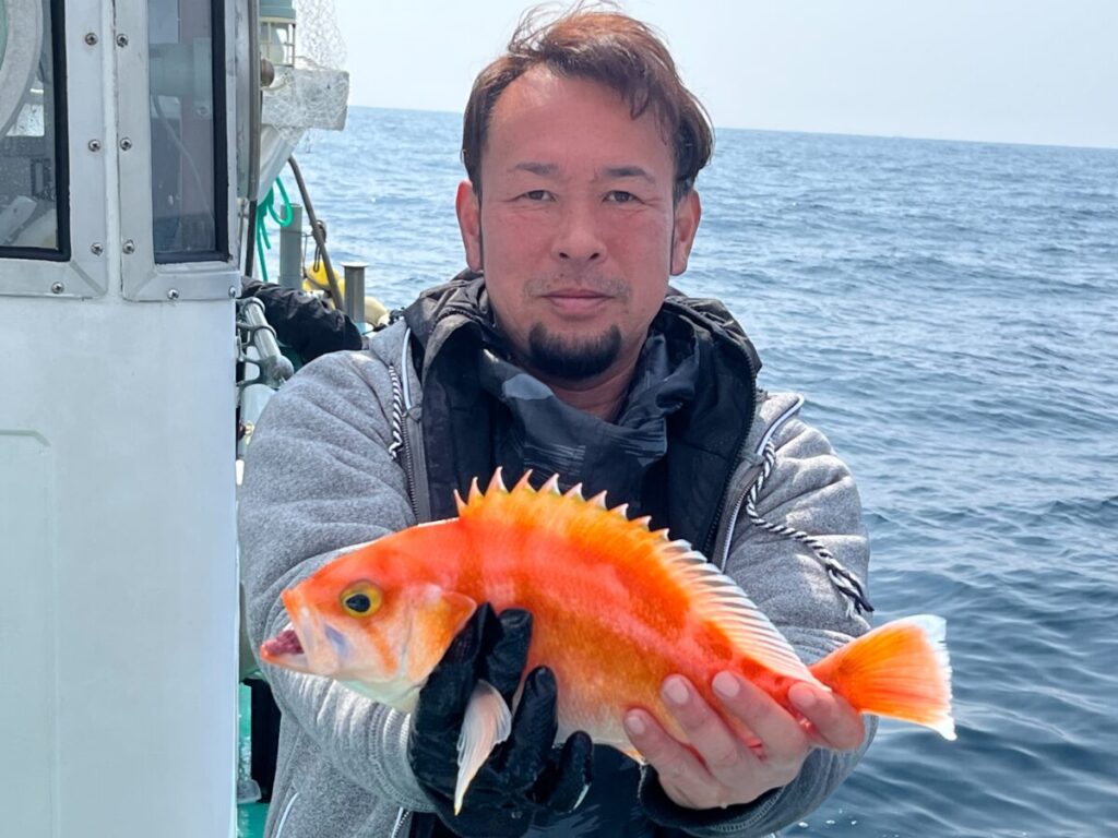 ボートに乗った人が、オレンジと黄色の色鮮やかな、とがったヒレの魚を手にしている。.