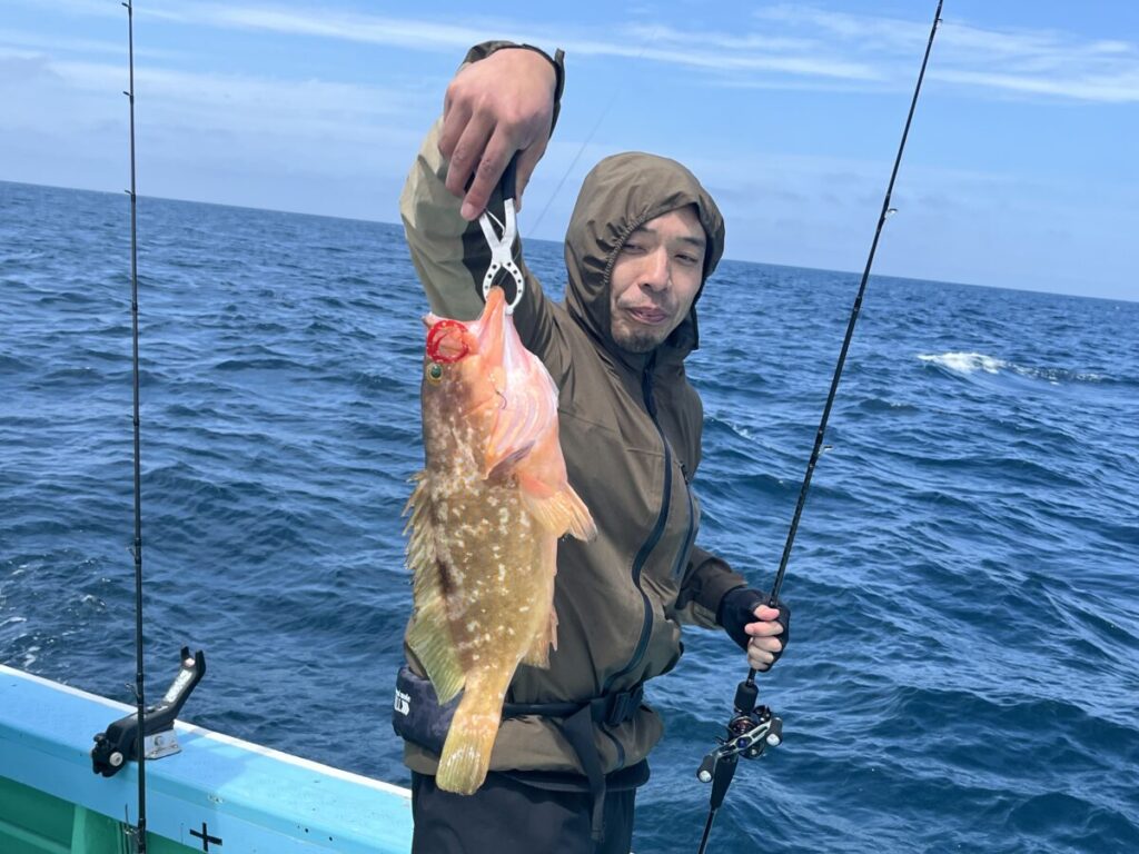 茶色のジャケットを着た人が、オレンジと黄色の模様のある大きな魚を掲げている。.