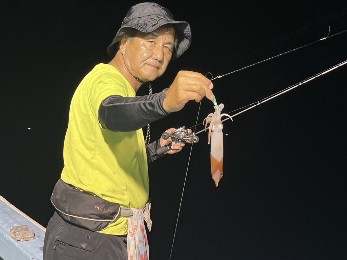 夜の船上で、釣り上げたイカを見せる釣り人