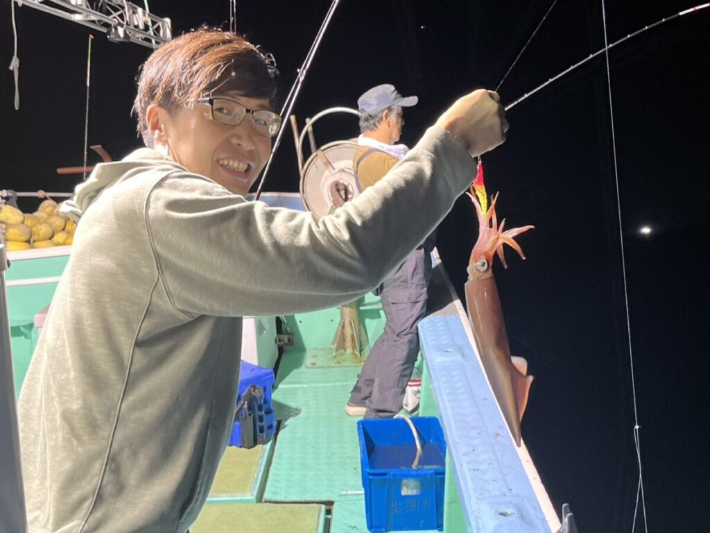 釣り上げたケンサキイカを手に笑顔を見せる釣り客。玄界灘・宗像大島沖の夜焚きイカ釣り