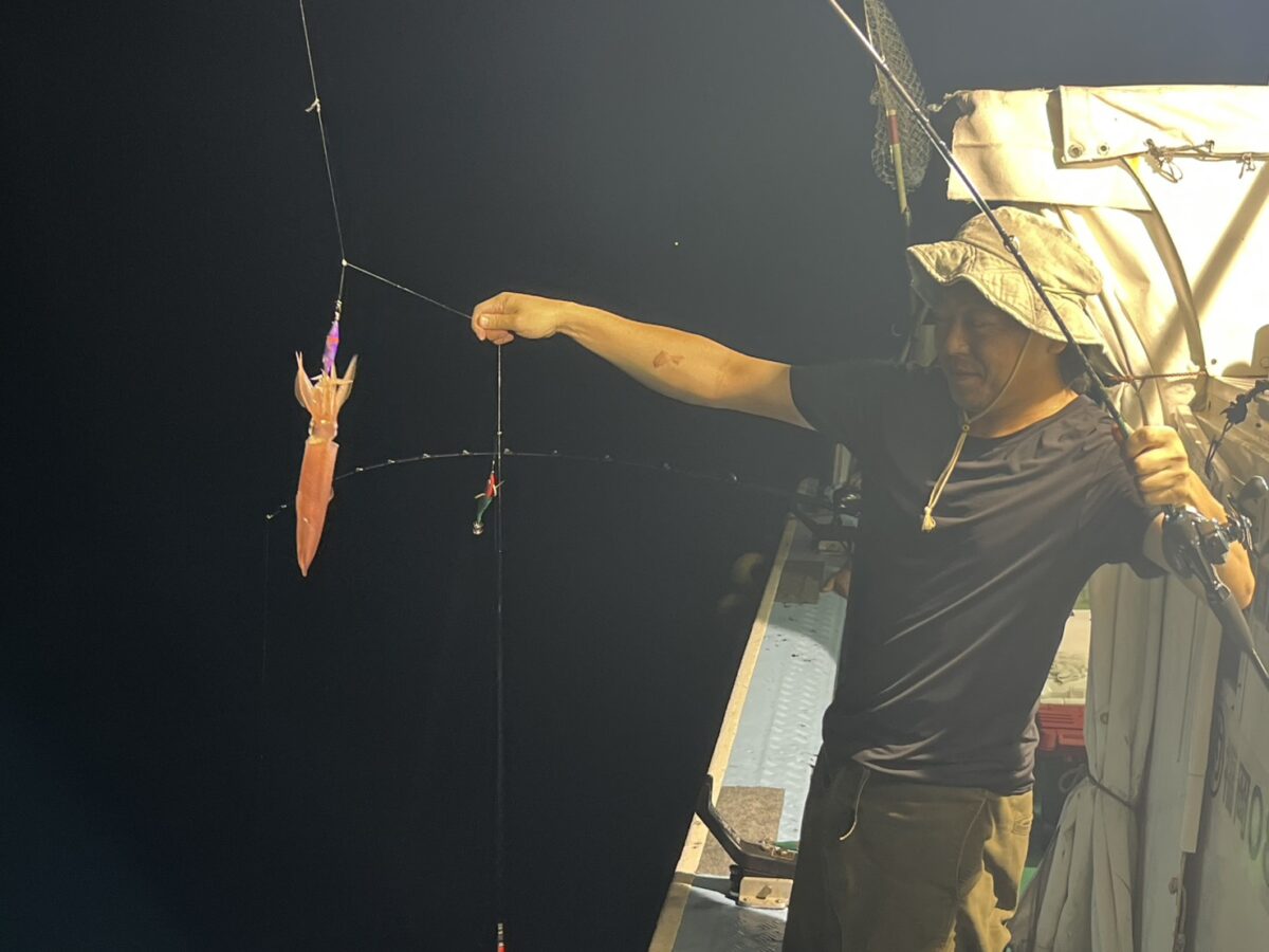 スッテに掛かった赤いケンサキイカを吊り上げて見せる釣り客。玄界灘・宗像大島沖の夜焚きイカ釣り