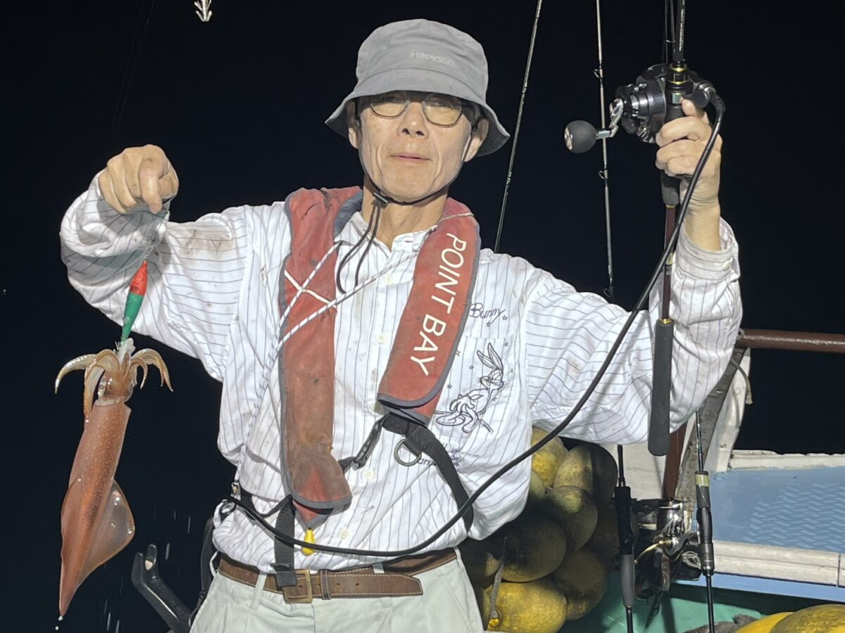 ライフジャケットを着けて釣り上げたケンサキイカを掲げる釣り客。若潮丸の夜焚きイカ釣り