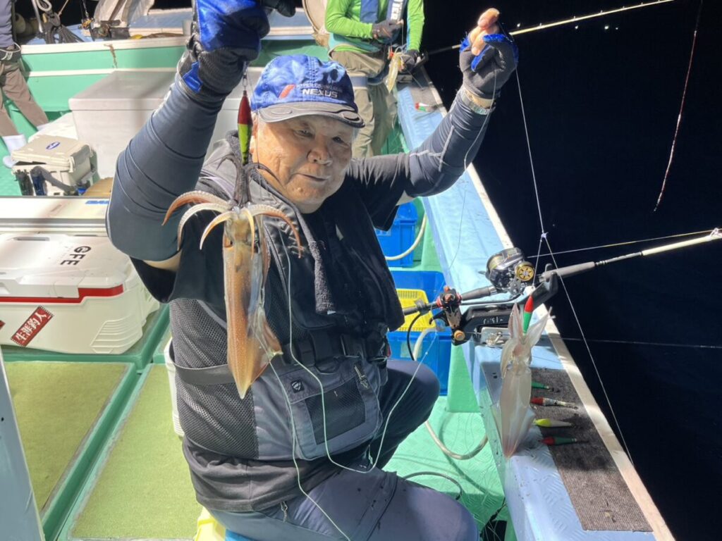 仕掛けに掛かった2杯のケンサキイカを掲げる釣り客。若潮丸の夜焚きイカ釣り