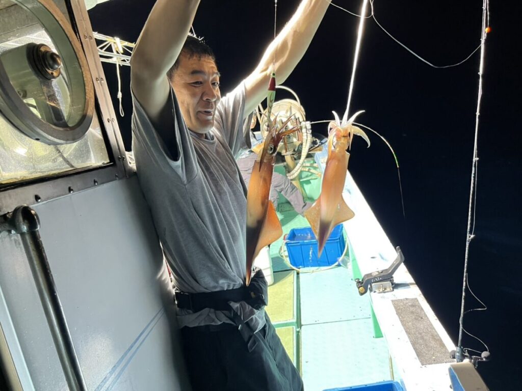 仕掛けに掛かった2杯のケンサキイカを掲げる釣り客。若潮丸の夜焚きイカ釣り