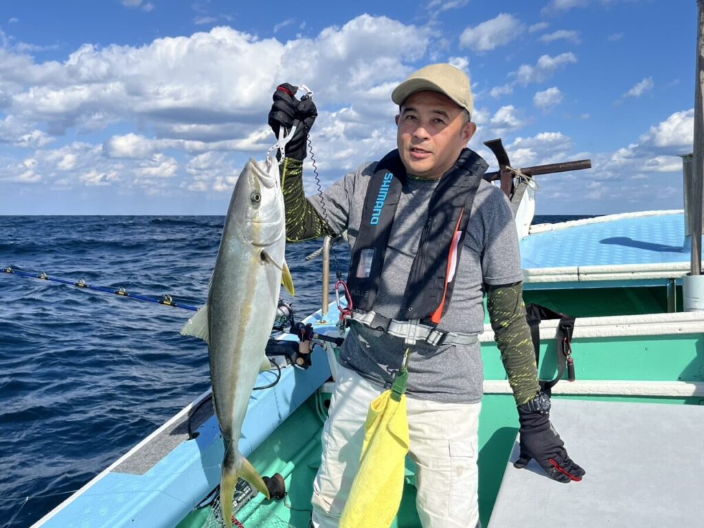 釣り上げた青物を掲げる釣り客。玄界灘・宗像大島沖、若潮丸の落とし込み釣り